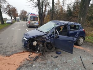 Uszkodzony po wypadku samochód w tle karetka pogotowia. Na jezdni rozsypany granulat do zbierania plam oleju z pojazdów.