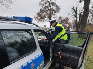 Zdjęcie radiowozu policyjnego i funkcjonariusza policji pracującego na miejscu wypadku. W tle karetka pogotowia.