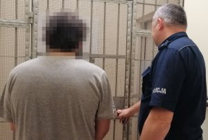 Zdjęcie policjanta z zatrzymanym mężczyzną przed kratami.