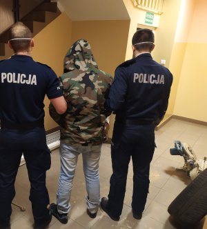 dwóch policjantów trzyma zatrzymanego mężczyznę ubranego w kurtkę moro na terenie komisariatu policji w Prabutach obok po prawej stronie odzyskane elektronarzędzia