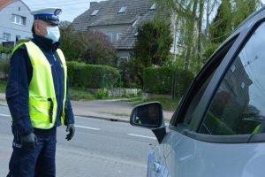 policjant w założonej maseczce stoi na poboczu obok niego radiowóz