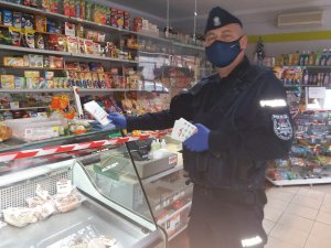 zdjęcie przedstawia umundurowanego policjanta mającego na sobie maseczkę który kładzie na ladzie sklepowej ulotki