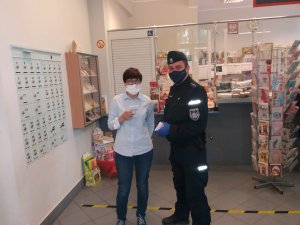umundurowany policjant przekazuje pracownikowi poczty polskiej ulotki dotyczące bezpieczeństwa na wypadek podejrzenia zarażenia się koronawirusem, oboje mają założone maseczki ochronne