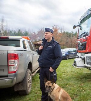 pomiędzy samochodami stoi policjant z psem służbowym