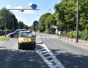 zdjęcie ulicy grunwaldzkiej  na której stoi żółty samochód z wybitą szybą za nim samochód straży miejskiej nad autami duży znak informujący o przejściu dla pieszych
