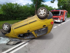 na środku ulicy widać żółte auto osobowe które leży na dachu za nim stoi wóz strażacki