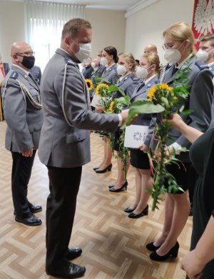 zdjęcie z obchodów święta policji w kwidzyńskiej jednostce przedstawia ono funkcjonariuszki stojące jedna obok drugiej naprzeciw stoją dwaj mężczyźni komendanci jednostki którzy wręczają akty mianowania i kwiat w postaci słonecznika