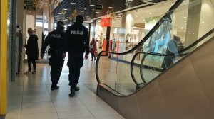 zdjęcie przedstawiające dwóch umundurowanych funkcjonariuszy idących po galerii handlowej w ramach działań mających na celu przeciwdziałanie rozprzestrzenianiu się choroby covid 19