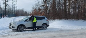 zdjęcie w zimowej scenerii, policjantka stoi przy oknie kierowcy zatrzymanego do kontroli i kontroluje jego dokumentację.