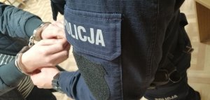 na zdjęciu widać policjanta w umundurowaniu który zakłada kajdanki na ręce osoby zatrzymanej