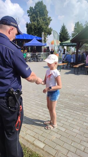 zdjęcie przedstawia funkcjonariusza policji wręczającego dziecku opaskę odblaskową w ramach akcji kręci mnie bezpieczeństwo nad wodą podczas festynu w miejscowości Ryjewo