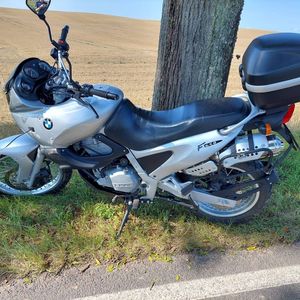 zdjęcie przedstawia motocykl koloru srebrnego marki bmw, którym poruszał się nieletni, motocykl postawiony jest na poboczu obok drzewa w tle widać zabronowane pole. Motocykl ma widoczne otarcia i urwane  kierunkowskazy.