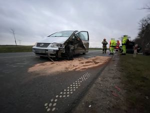 na ulicy stoi rozbity podczas kolizji samochód koloru srebrnego z uszkodzoną prawą przednią lampą i prawym nadkolem z uwagi na wycieki płynów eksploatacyjnych strażacy posypali jezdnię pomarańczowym piaskiem neutralizującym te wycieki w tle widać stoijących strażaków i osoby z uszkodzonego auta