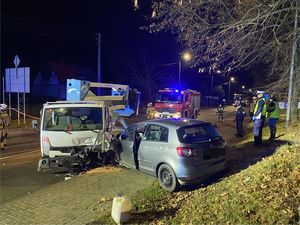 zdjęcie z miejsca wypadku na którym widać samochód z podnośnikiem który zderzył się z samochodem osobowym po prawej stronie stoją policjanci którzy pracują na miejscu tego zdarzenia w tel wóz strażacki