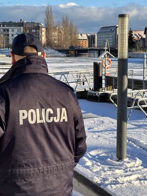na zdjęciu widać stojącego tyłem do fotografa policjanta który patrzy w stronę zbiornika wodnego który pokryty jest lodem