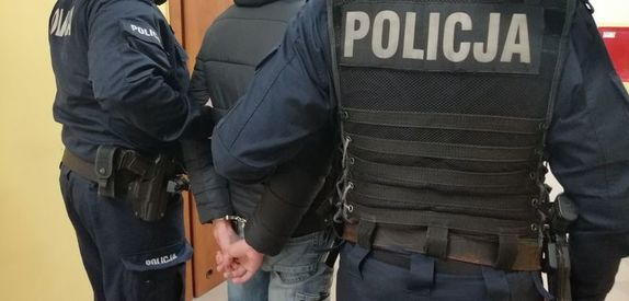 dwóch policjantów prowadzi zatrzymanego mężczyznę zakutego w kajdanki