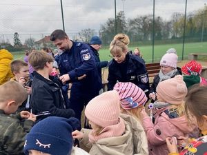 na zdjęciu widać policjanta i policjantkę którzy otoczeni są gromadą dzieci którym wręczają opaski odblaskowe