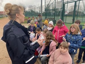 na zdjęciu widać policjantkę która otoczona jest gromadą dzieci którym wręcza opaski odblaskowe