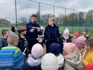 na zdjęciu widać policjanta i policjantkę którzy otoczeni są gromadą dzieci którym wręczają opaski odblaskowe