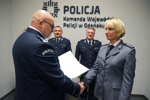 na pierwszym planie zdjęcia widać jak umundurowany policjant wręcza policjantce dokument w tle widać kolejnych dwóch umundurowanych policjantów za nimi na ścianie napis komenda wojewódzka policji w gdańsku