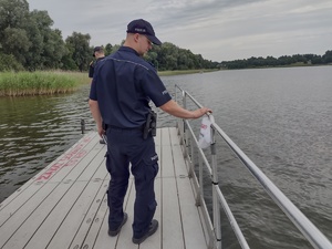 na zdjęciu widać policjanta idącego pomostem który jest na wodzie