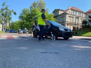 na zdjęciu widać stojący na jezdni na przejściu samochód osobowy w jego kierunku idzie policjant który mierzy odległość od krawężnika do samochodu