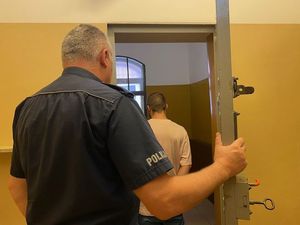 na zdjęciu widać policjanta który trzyma drzwi od celi w której stoi odwrócony tyłem do fotografa mężczyzna