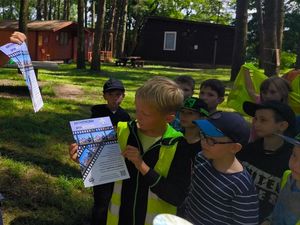 na zdjęciu widać chłopca który trzyma w ręku plakat do akcji kręci mnie bezpieczeństwo obok niego stoją inni chłopce w tle widać fragment lasu i domku drewniane