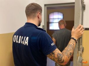 na zdjęciu widać policjanta który otwiera drzwi do celi w progu której stoi zatrzymany mężczyzna