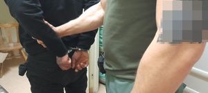 na zdjęciu widać nieumundurowanego policjanta który trzyma za rękę zakutego w kajdanki sprawcę kradzieży rozbójniczej