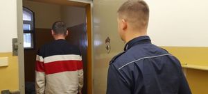 zdjęcie policjanta stojącego w drzwiach celi a przed nim zatrzymany za jazdę po alkoholu mężczyzna