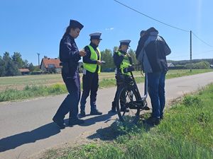 na zdjęciu widać trzy policjantki które dokonują kontroli drogowej rowerzysty w tle widać łąkę i las