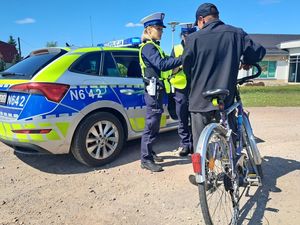 na pierwszym planie widać mężczyznę który który trzyma rower obok siebie tuż obok stoją dwie policjantki przy radiowozie mężczyzna dmucha w alkomat w tle widać budynek banku