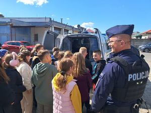 na zdjęciu widać policjanta który stoi na parkingu policyjnym przy grupie dzieci które oglądają policyjny radiowóz