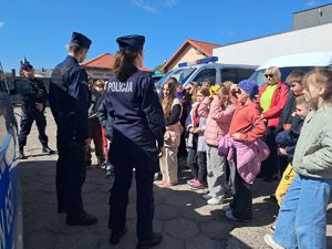 na zdjęciu widać stojących tyłem do fotografa policjantów którzy opowiadają dzieciom o swojej pracy w tle widać radiowóz
