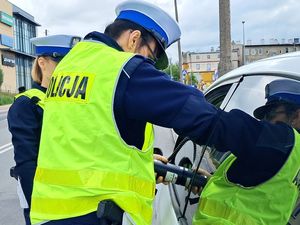 na zdjęciu widać policjantkę stojącą przy otwartym oknie kontrolowanego samochodu która przykłada urządzenie do mierzenia przejrzystości szyb