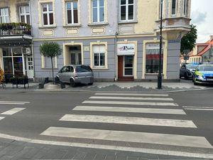 na zdjęciu widać jedną z kwidzyńskich ulic na której doszło do kolizji drogowej widać na tym zdjęciu samochód stojący na chodniku który uderzył w budynek obok są ławki w tle po prawej stronie zdjęcia widać policyjny radiowóz