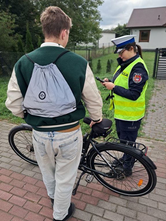 na zdjęciu widać policjantkę dokonującą legitymowania młodego mężczyzny który jechał rowerem dostał on od niej woreczek odblaskowy