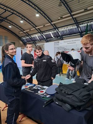 na zdjęciu widać uczniów w mundurach swojej szkoły którzy stoją przy stoisku kwidzyńskich policjantów i oglądają prospekty dotyczące doboru do Policji obok nich stoi policjantka