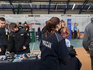 na zdjęciu widać uczniów w mundurach swojej szkoły którzy stoją przy stoisku kwidzyńskich policjantów i oglądają prospekty dotyczące doboru do Policji obok nich stoi policjantka