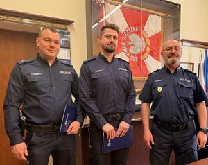 na zdjęciu widać trzech umundurowanych funkcjonariuszy z których dwóch otrzymało awans jeden to komendant za ich plecami jest gablota w której wisi sztandar policji