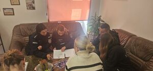 na zdjęciu widać siedzących na kanapach troje policjantów którzy przeglądają rozłożoną na stole dokumentacje osób chcących wstąpić w szeregi policji na przeciwko policjantów siedzi dwoje młodych ludzi