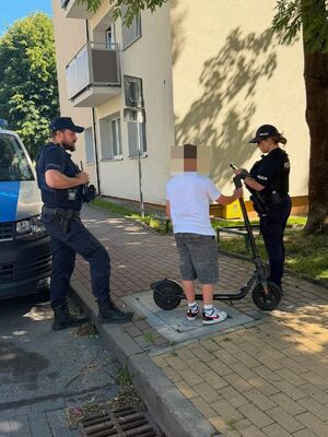 na zdjęciu widać dwoje funkcjonariuszy którzy legitymują chłopca i przypominają mu przepisy związane z użytkowaniem hulajnogi elektrycznej która obok niego stoi