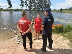 na zdjęciu widać policjantkę rozmawiającą na brzegu kąpieliska plaży z ratownikami wodnymi