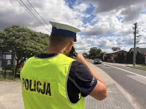 na zdjęciu widać policjanta który mierzy prędkość nadjeżdżającego auta