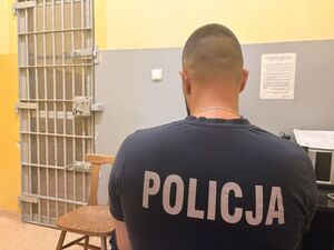 na zdjęciu widać policjanta siedzącego przy biurku przed nim widać drzwi do celi