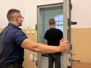 na zdjęciu widać policjanta który otwiera drzwi do celi w której progu stoi zatrzymany mężczyzna