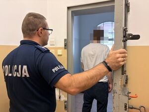 na zdjęciu widać policjanta który otworzył drzwi do celi w progu której tyłem do aparatu stoi osadzony w niej mężczyzna