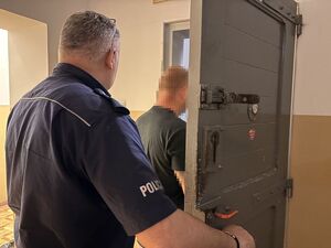 na zdjęciu widać zatrzymanego mężczyznę który stoi w drzwiach celi przed nim jest umundurowany policjant