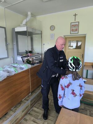 na zdjęciu widać policjanta który zakłada kask rowerowy dziecku na głowę
